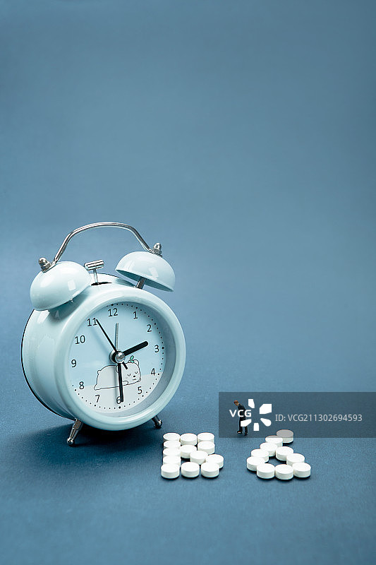 闹钟旁边用褪黑素摆成的维生素B6按时入睡图片素材