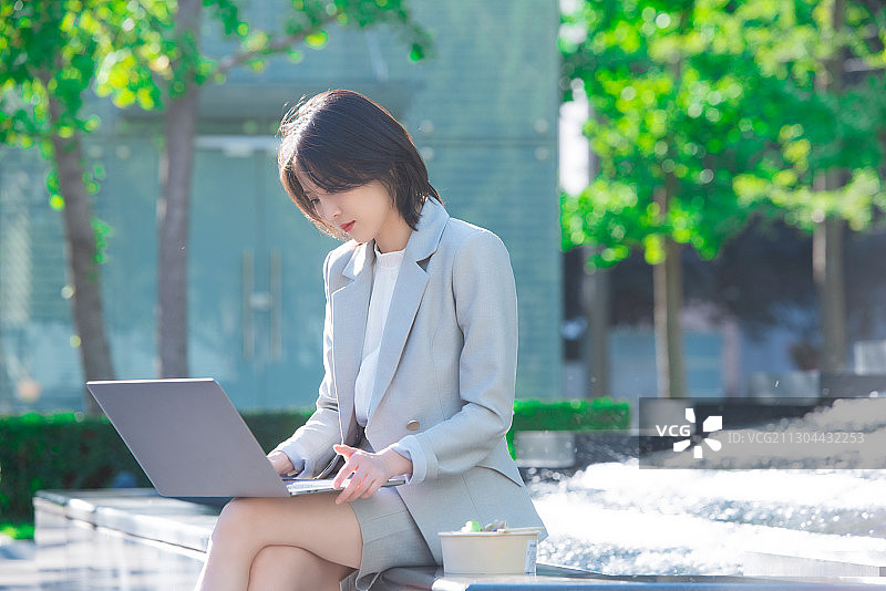 商务女性坐着户外边吃饭边工作图片素材
