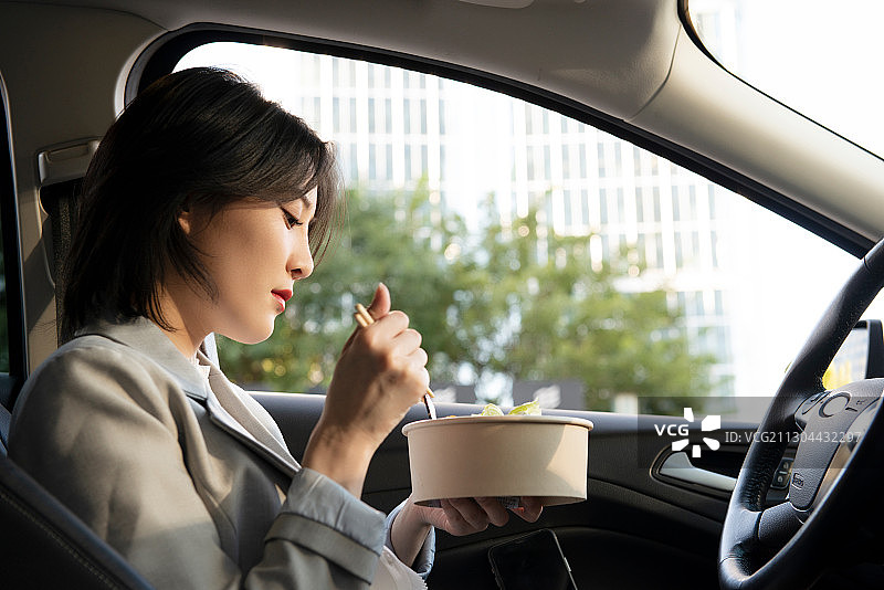 商务女性坐着车内边吃饭边工作图片素材