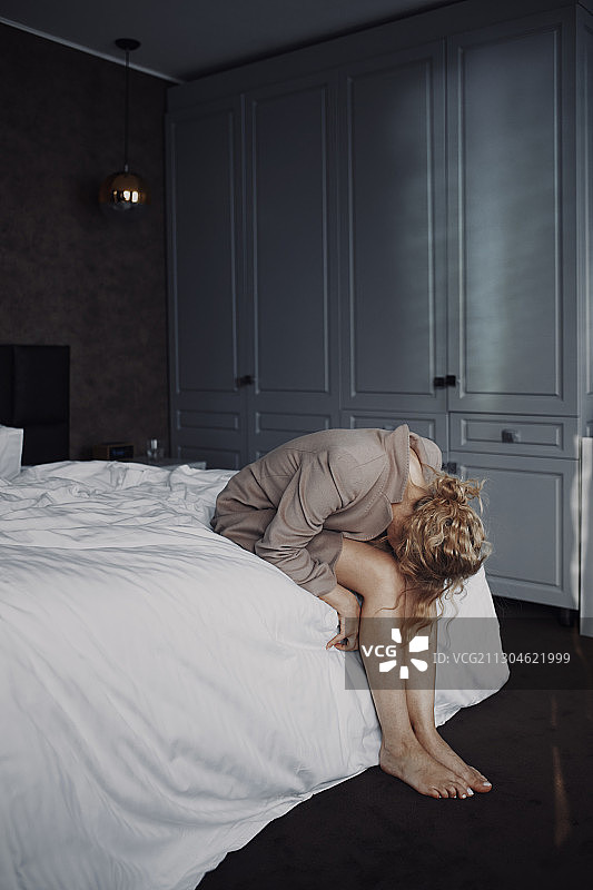 沮丧的金发女人面朝下跪在未整理的床上，呈胎儿姿势。非常适合做书的封面图片素材