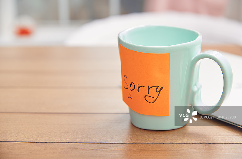 笔记本电脑旁土耳其色咖啡杯上的橙色“抱歉”便签图片素材