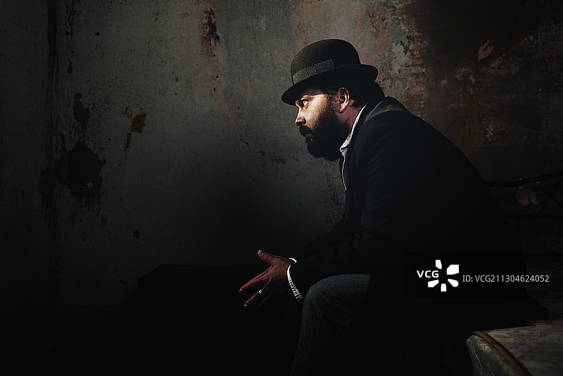 19世纪风格的蓄胡男子身穿西装和圆顶礼帽坐在床上图片素材