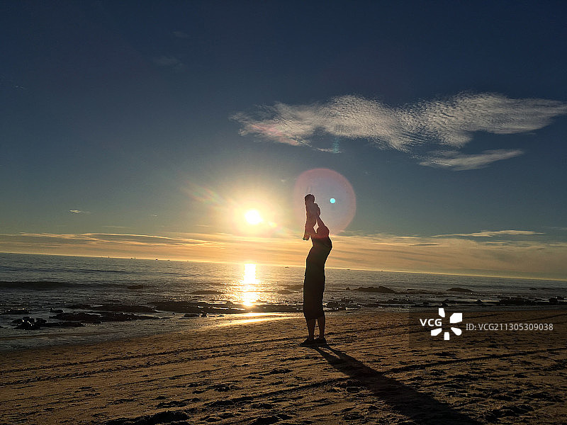 大海边 迎着落日的余晖一位父亲高高举起手中的孩子图片素材