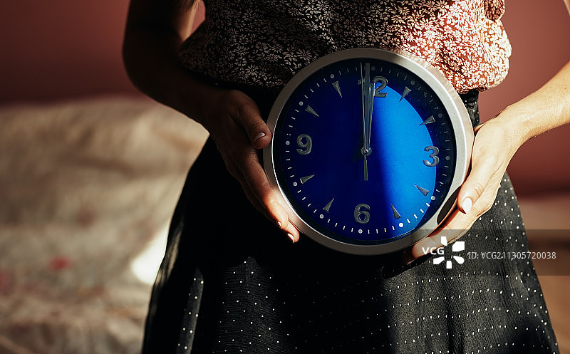 拿着显示中午12点的蓝色圆形时钟的匿名女子，适合做书籍封面图片素材