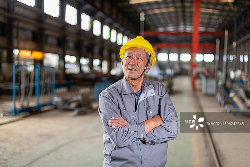车间里双臂交叉抱于胸前带安全帽的老工人图片素材