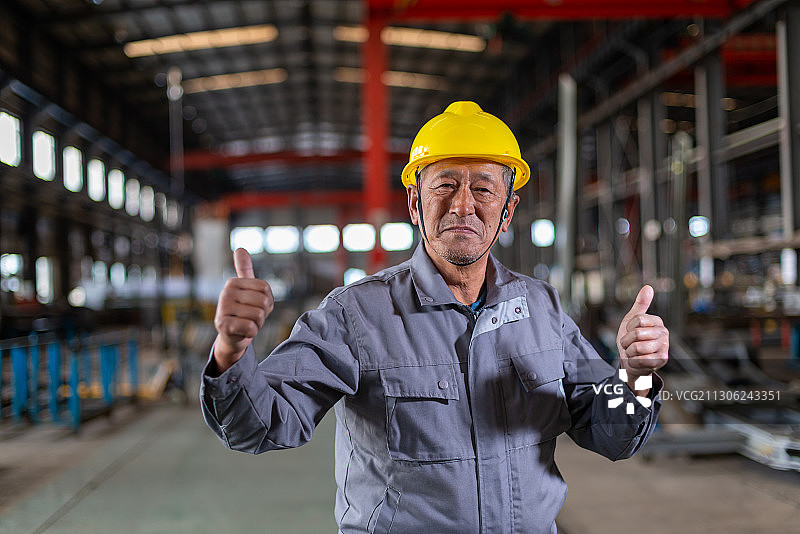 车间里双手伸出大拇指的带安全帽微笑的老工人图片素材