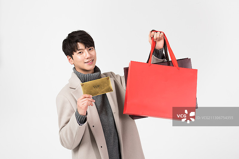 穿着冬装，拿着礼券和购物袋微笑的男人图片素材
