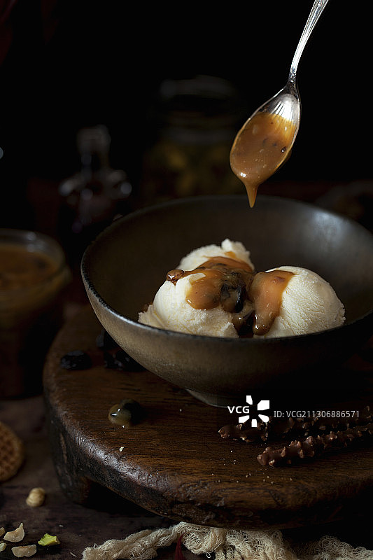 焦糖酱从勺子上淋到碗里的香草冰淇淋上图片素材