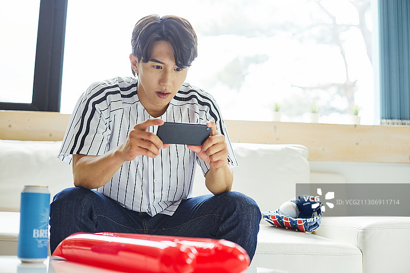 男人在客厅沙发上用智能手机看棒球比赛，欢呼雀跃，期待手游图片素材