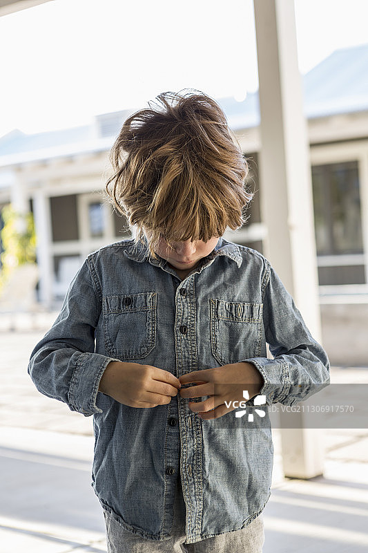 正在扣牛仔衬衫的6岁男孩图片素材