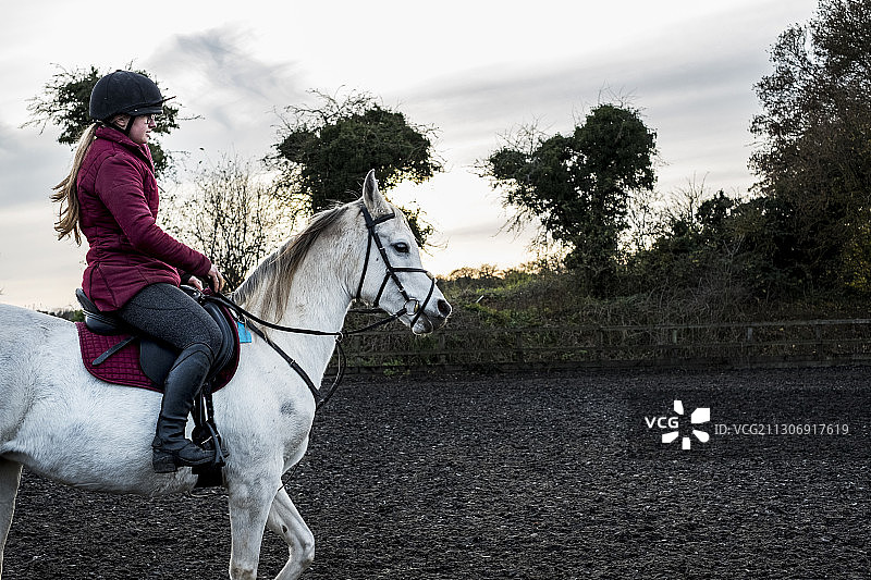 年轻女子在围场里骑白色科布马图片素材