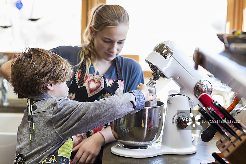 13岁少女和6岁弟弟在厨房里使用搅拌碗图片素材