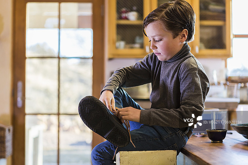 坐在高脚凳上穿靴子的六岁男孩图片素材