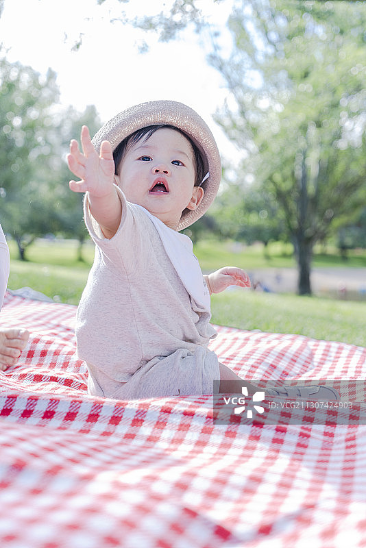 戴着遮阳帽坐在野餐垫上晒太阳的男婴图片素材