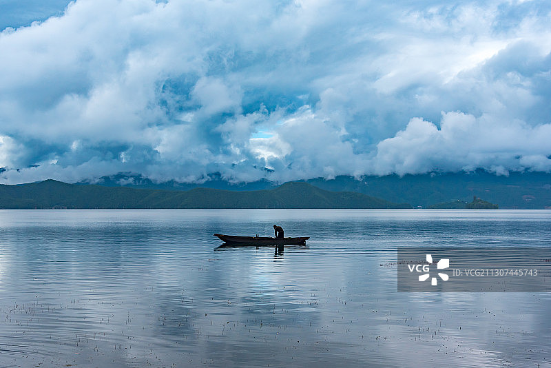 云南泸沽湖上的一叶扁舟，蓝天白云倒映在平静的水面上图片素材