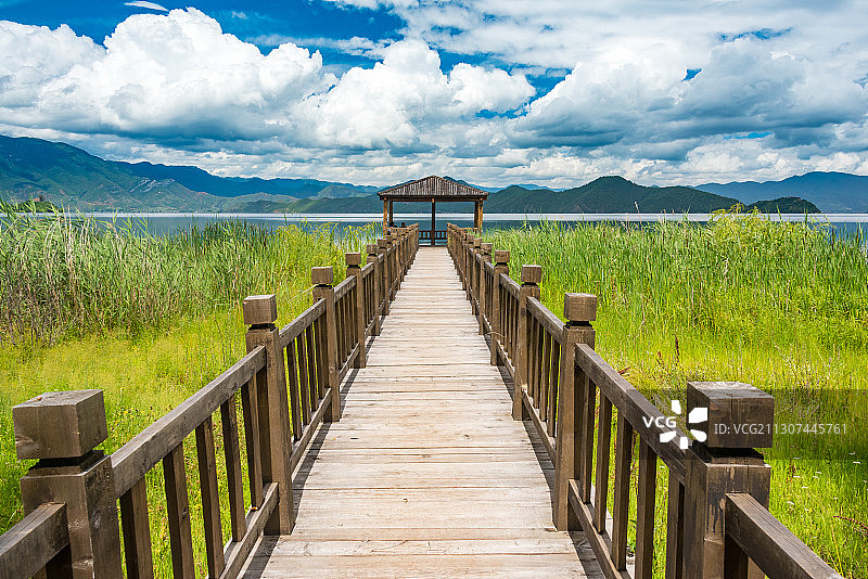 蓝天白云下的泸沽湖边，一条木栈道向远处延伸，尽头时一个木屋图片素材