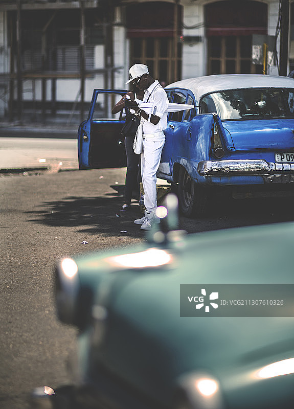 在停车场，两个人站在一辆20世纪50年代经典汽车的敞开的车门旁图片素材