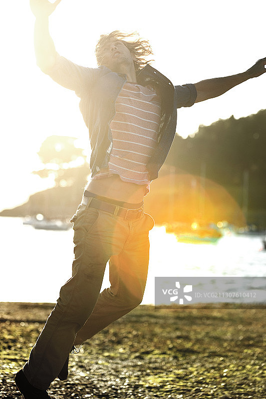 在卵石滩上跳跃，举起双臂的年轻人图片素材