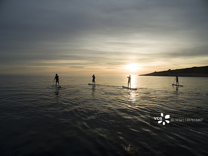 日落时分人们在桨板上划船的高角度照片图片素材