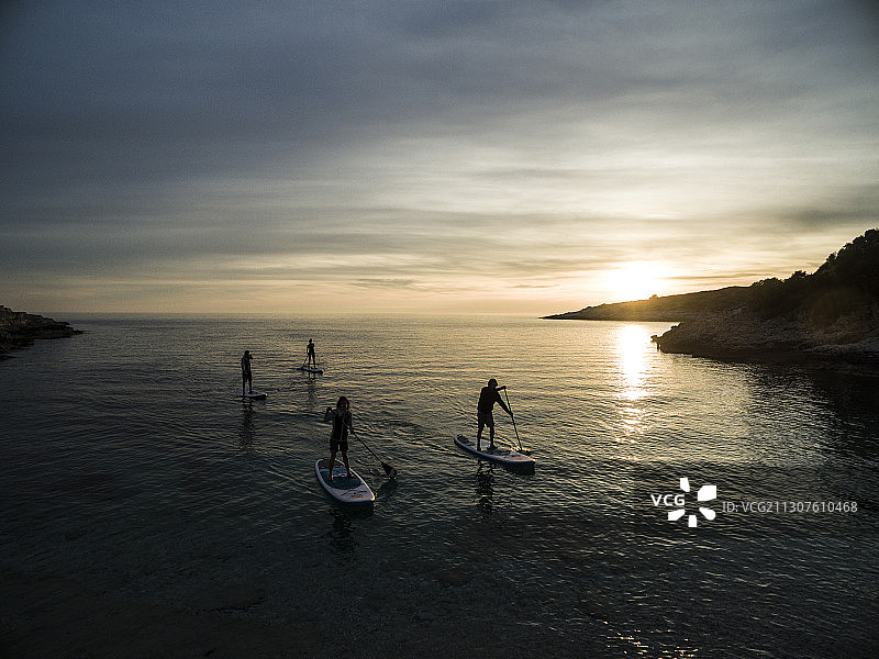 日落时分人们在桨板上划船的高角度照片图片素材