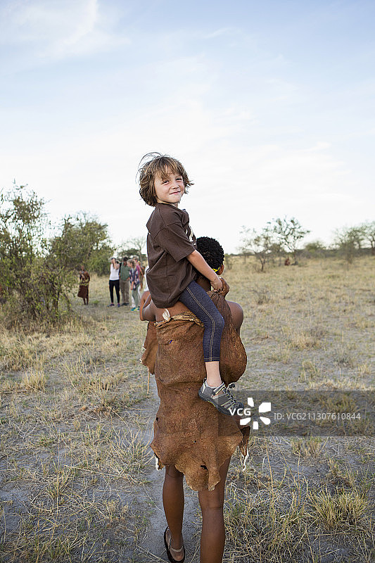 五岁男孩骑在 San 布须曼人的肩膀上图片素材