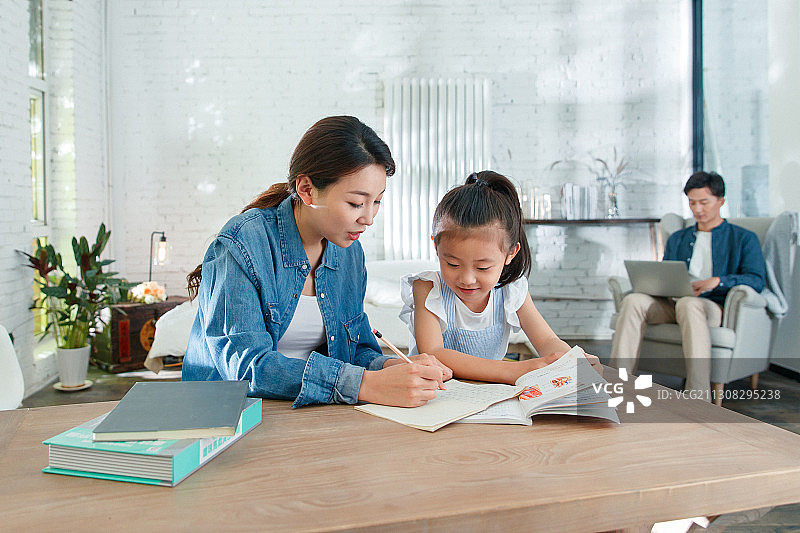 漂亮的青年女人辅导女儿写作业图片素材