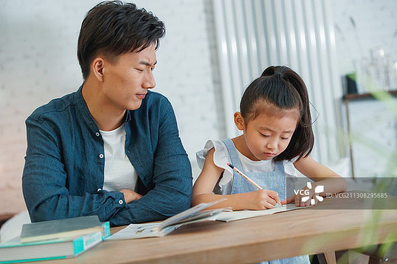 辅导女儿做作业的年轻爸爸图片素材