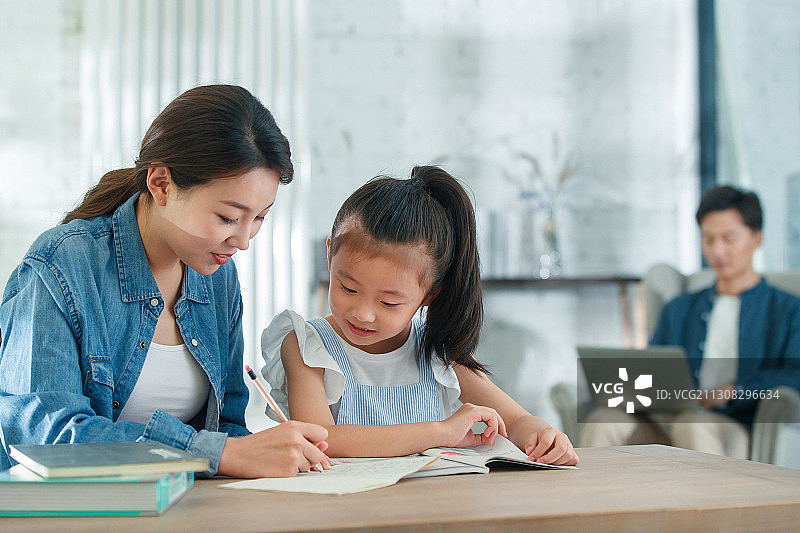 漂亮的青年女人辅导女儿写作业图片素材