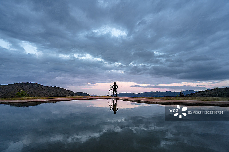 阴天水池边的一个拍摄男人及倒影图片素材