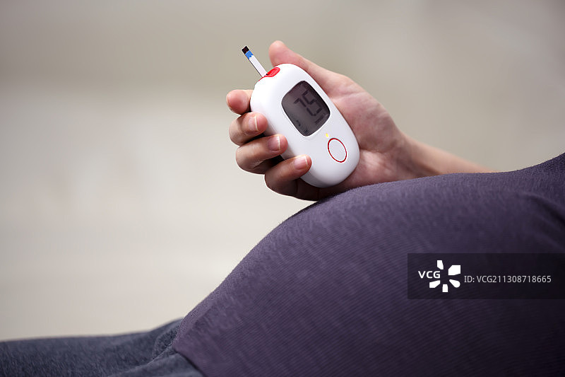 一个手拿血糖仪的孕妇肚子特写图片素材