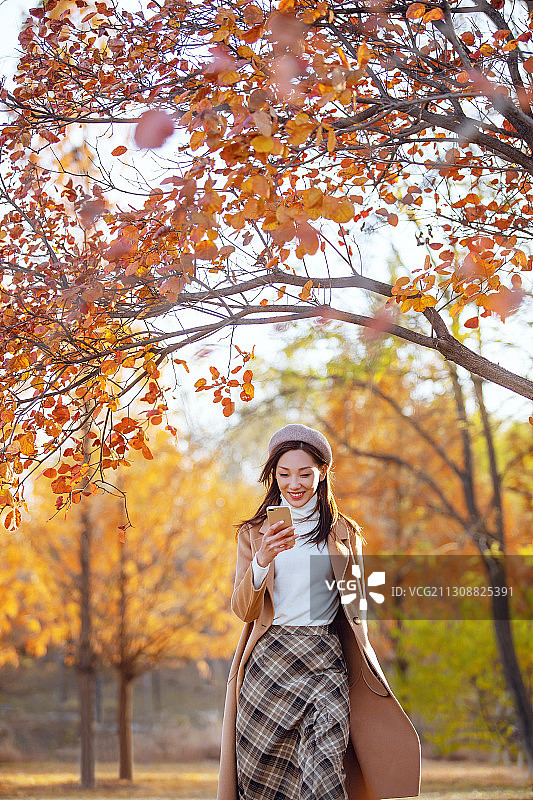 年轻女子在公园里走路看手机图片素材