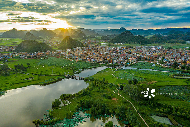 普者黑日出航拍，暖黄光束射向大地，田园村庄，水面倒映着蓝天图片素材