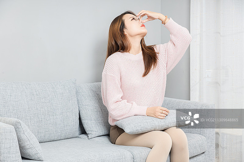 坐在沙发上,感觉鼻子难受的亚洲女孩图片素材