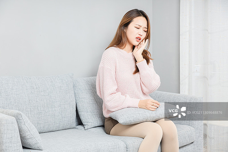 坐在沙发上,感觉牙疼的亚洲女孩图片素材