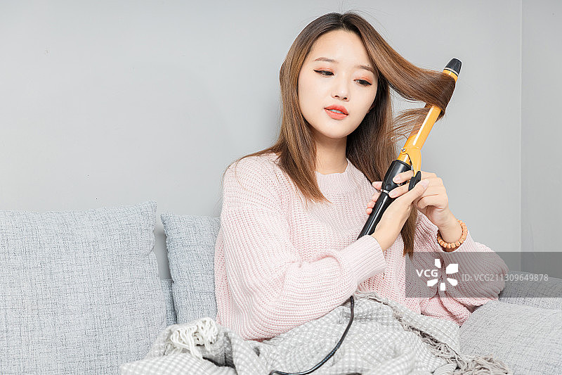坐在沙发上,正在卷头发的亚洲女孩图片素材