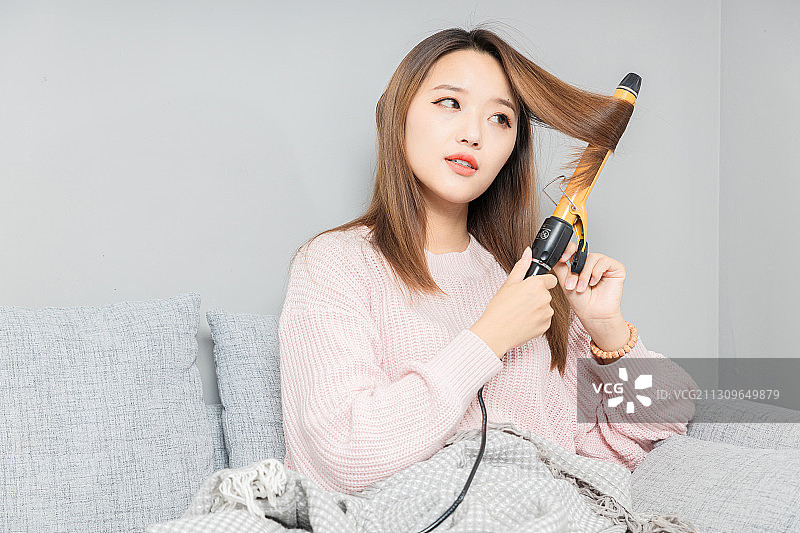 坐在沙发上,正在卷头发的亚洲女孩图片素材