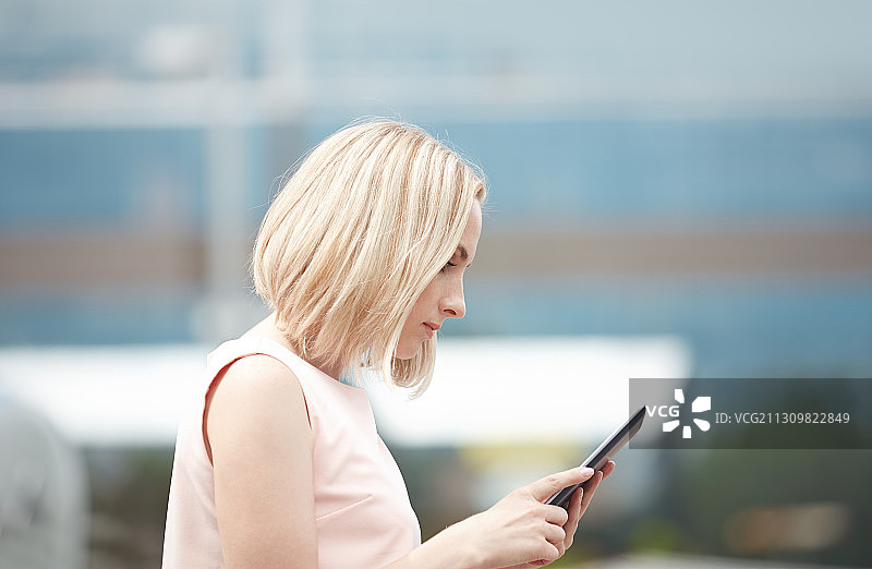 在市中心拿着平板电脑的金发女人图片素材