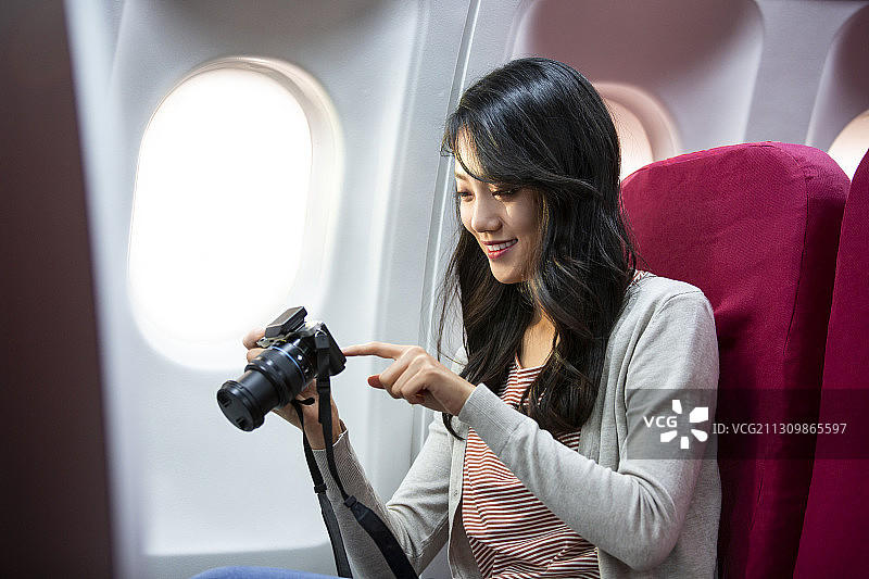 青年女子旅行度假在飞机机舱上看着相机里的照片图片素材