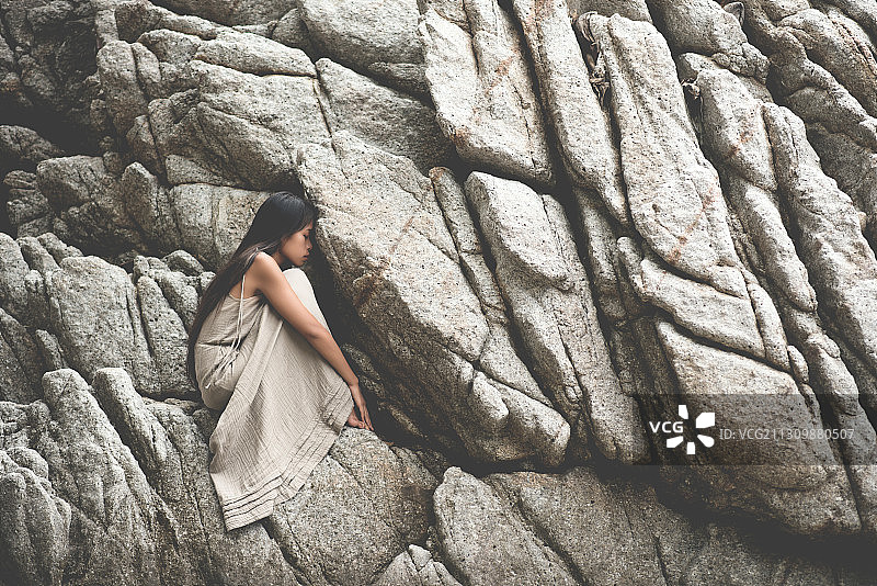 坐在泰国帕岸岛悬崖上的亚洲年轻女子侧视图图片素材