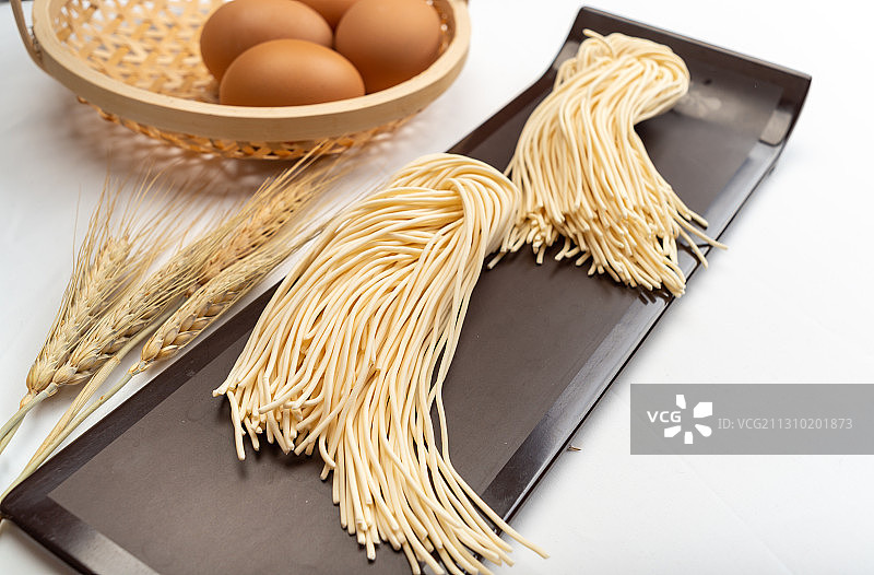 白色背景下盘子中的生食面条和竹篮中鸡蛋和麦穗图片素材