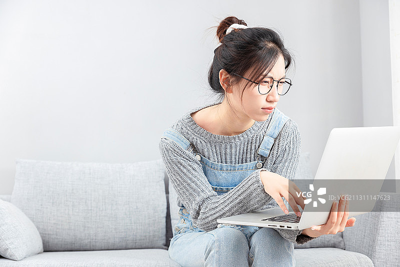 坐在沙发上戴着眼镜用电脑的亚洲女孩图片素材
