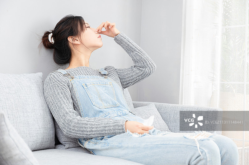 坐在沙发上感觉鼻子难受的亚洲女孩图片素材
