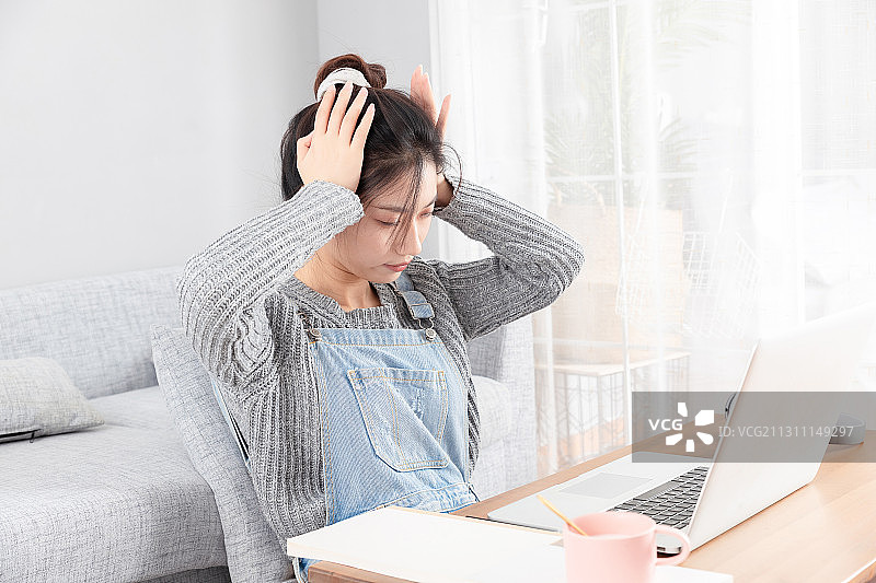 坐在地毯上，正在上网课并且头疼的亚洲女孩图片素材