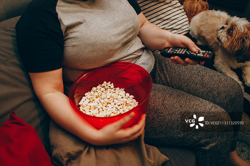 年轻夫妇与宠物狗和爆米花零食一起度过舒适的夜晚，巴西米纳斯吉拉斯州贝洛奥里藏特图片素材
