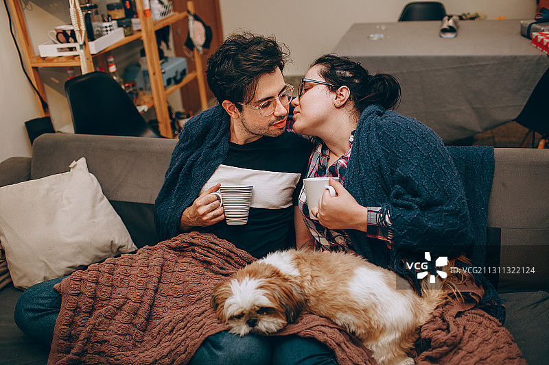 年轻的白人情侣在舒适的夜晚分享热饮，宠物狗相伴图片素材