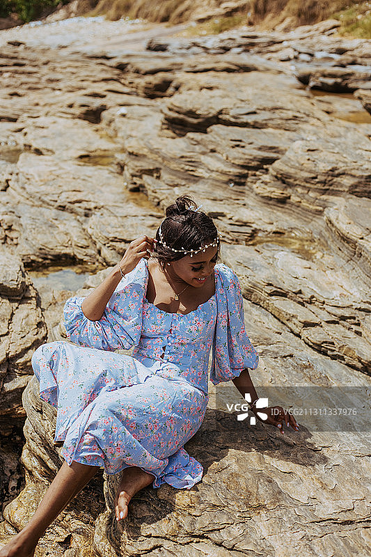 身穿连衣裙头戴花冠的圭亚那年轻女子坐在加纳阿克拉海滩的岩石上图片素材