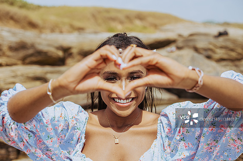 在加纳阿克拉海滩，圭亚那年轻女子身穿连衣裙，头戴花冠，用手摆出心形图片素材