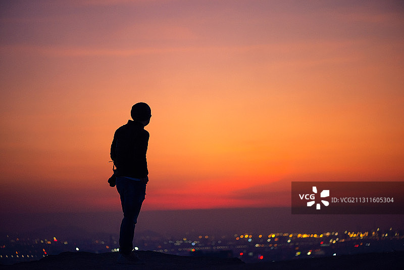 黄昏，霞光正盛，一个人在山上看着华灯初上的城市图片素材