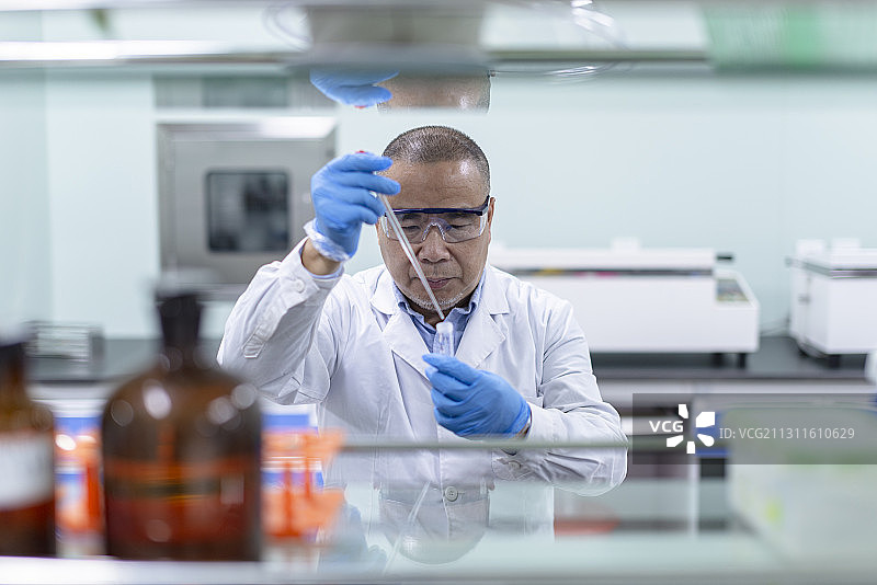 身穿白大褂的中年男性在医疗试验室内操作试验图片素材