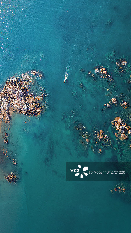 航拍从碧海浅滩的礁石群中驶过的游艇图片素材